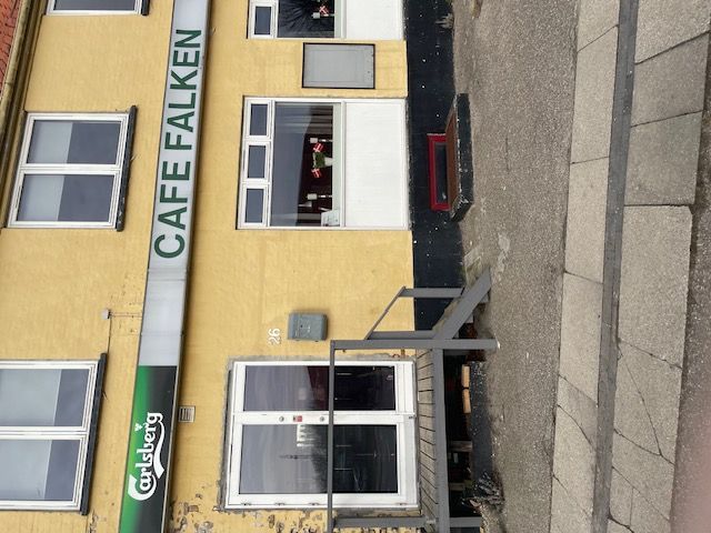 En gule bygning med teksten Café Falken og Carlsberg på facaden samt fire vinduer og et trætrin til indgangen