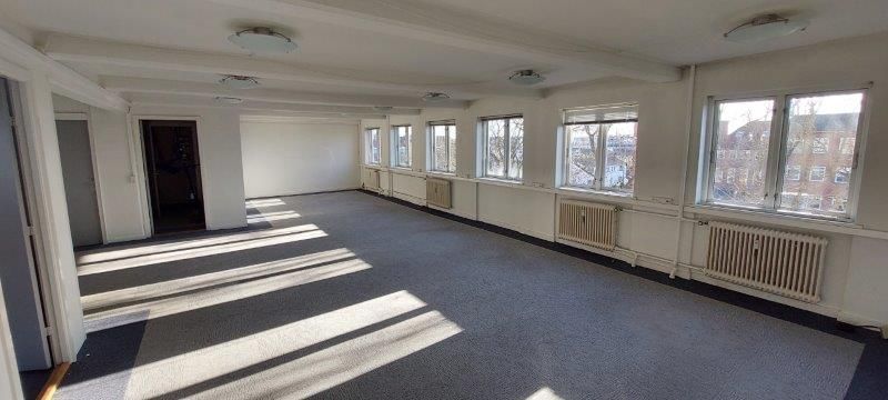 En stor og ren stue med hvide vægge, lysekroner, vinduer med gardiner og radiatorer i hvidt