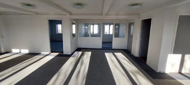 En stor og lys kontorbygning med hvide vægge, grå gulvbelægning, og mange vinduer. Solstråler skinner ind gennem vinduer og