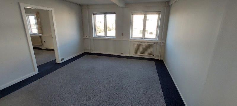 En tom kontor i hvid og blå farve med lysevinduer og radiatorer i hvidt.