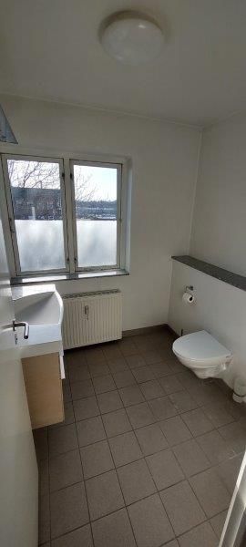 Et rent badeværelse med en hvid håndvask og en toilet på højre side og en radiator under vinduet