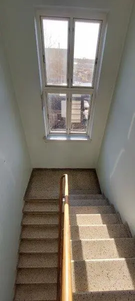 Træhåndtag på marmortrapper med sollys. Glasvindue og hvide vægge.