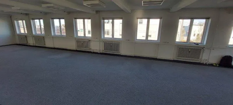 Rummeligt kontor med højt til loftet og store vinduer, hvor man ser ud på bygninger og grønne træer