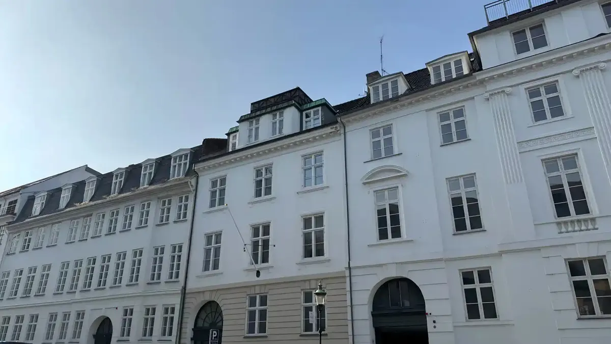 Kontorbyggeri med hvide facader og vinduer i klassisk stil med lysegrå gesims og en stor bueformet indgang