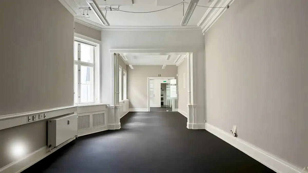 Et kontorlokal med højt til loftet og lyse, smukke vinduer med udsigt til gaden. Ingen mennesker er synlige, og der er høj
