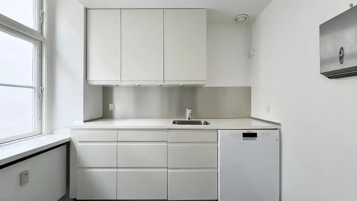 Rent og funktionelt køkken med hvide skabsfronter og metalbælte over vaskemaskine og spisestue.