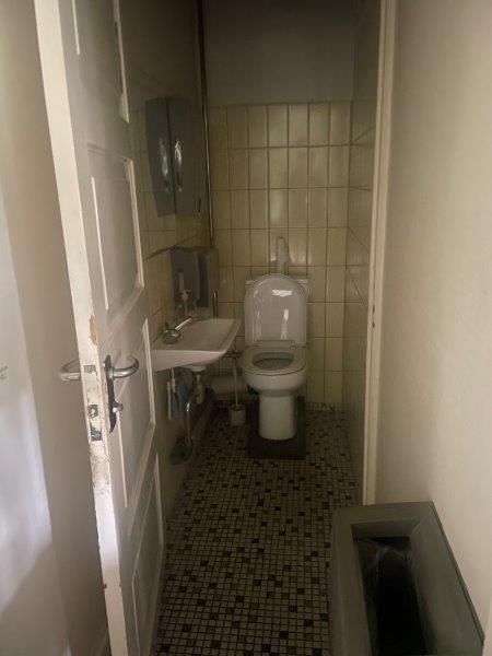 Ren toiletrum med toilet, håndvask, håndsæbe og gulv med mønstret fliser og hvid ventilkasse