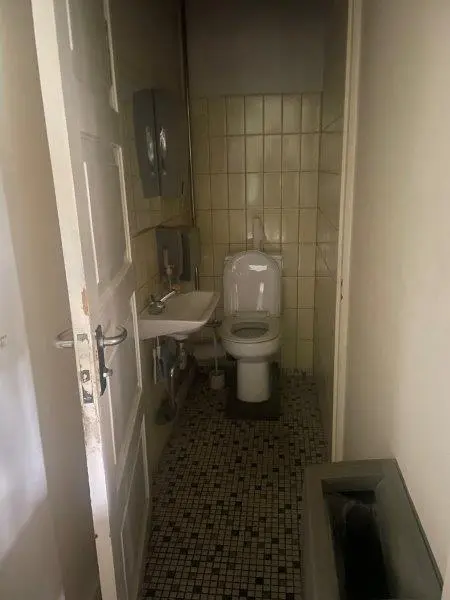 Ren toiletrum med toilet, håndvask, håndsæbe og gulv med mønstret fliser og hvid ventilkasse