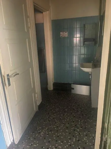 En tom værelse med hvide vægge, gult loft, sort-hvide mønstre på gulvet, hvidt dørblad og gule dørbeslag, hvidt badeværelse