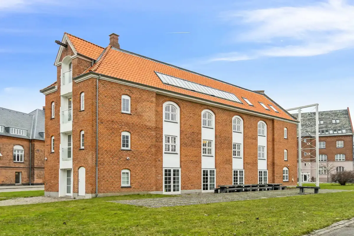 Moderne røde mursten og hvide vindueskarme på en bygning med solfanger på taget. Bygningen ligger på en grøn plæne med to