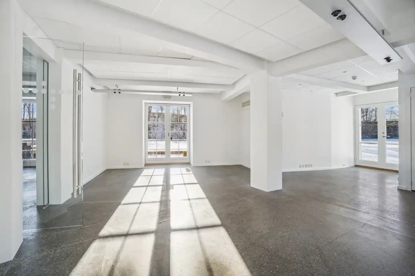 Moderne kontor med højt til loftet, hvide vægge, glasdøre og cementgulv