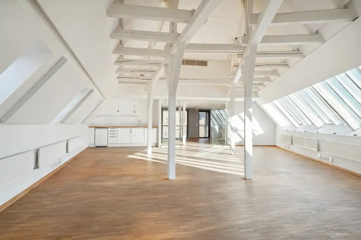 Lyst rum med lyse trægulve og loft. Høje vinduer giver masser af lys og udsigt til byen.