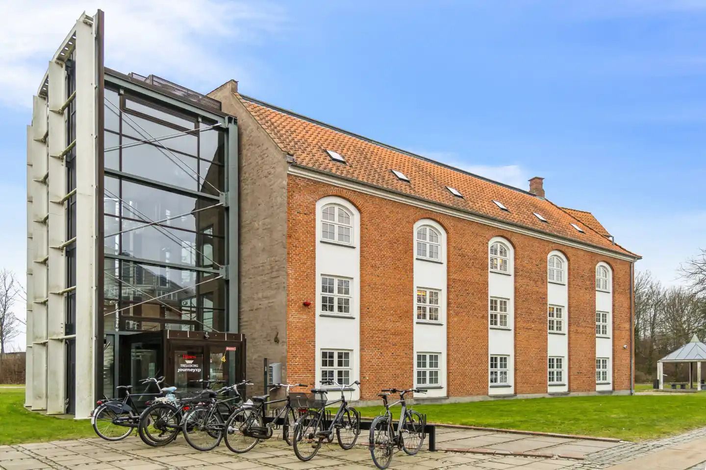 Fire cykler står parkeret foran bygningen med røde mursten og glasvinduer