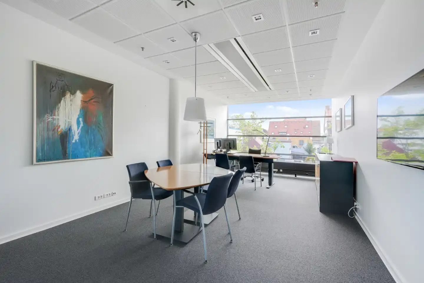 Kontor med bord, stole, skrivebord, computer, lampe og malerier på væggen med udsigt til byen fra vinduet