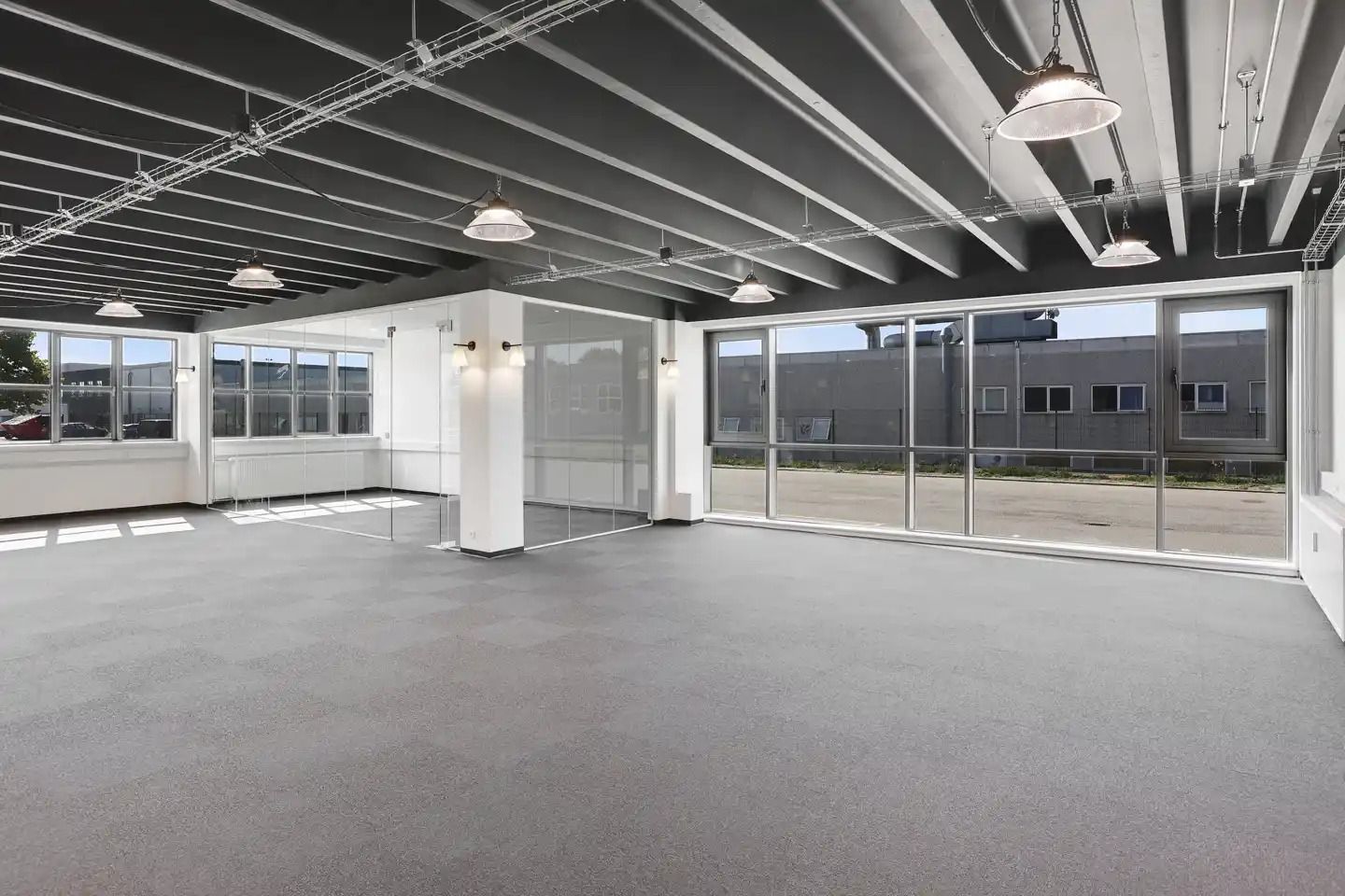 Store lagerlokaler med højloft, hvide vægge, store vinduer, og lyse loftslampe. Ingen mennesker er synlige på billedet.