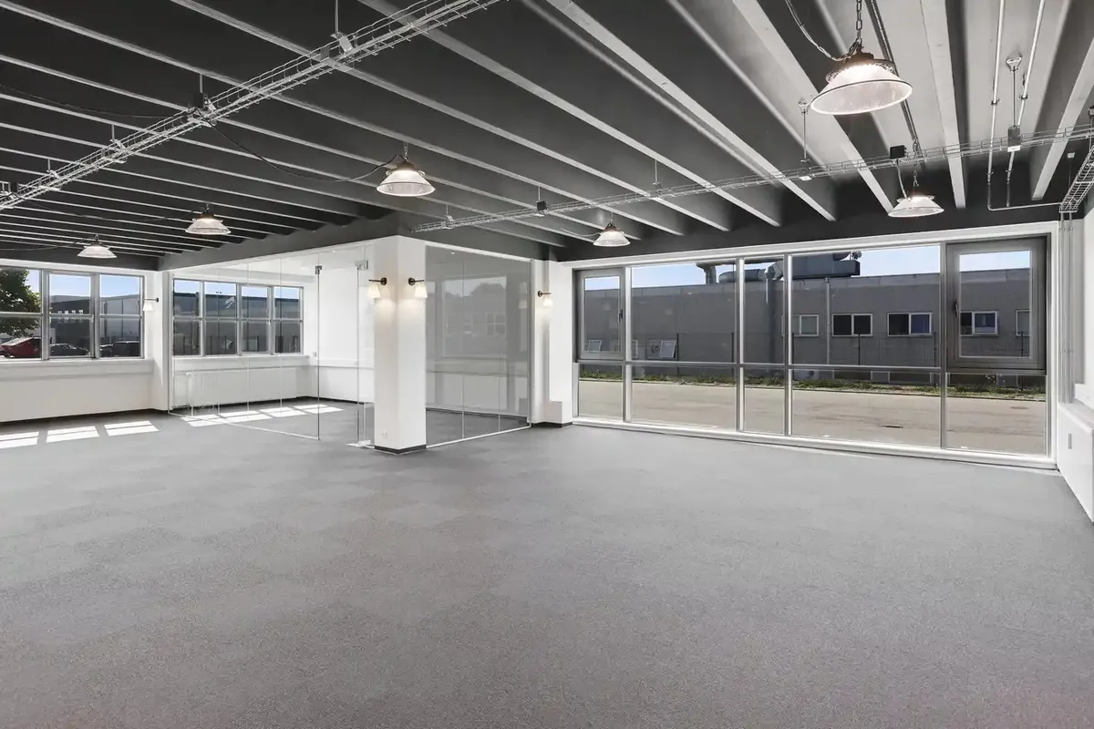 Store lagerlokaler med højloft, hvide vægge, store vinduer, og lyse loftslampe. Ingen mennesker er synlige på billedet.