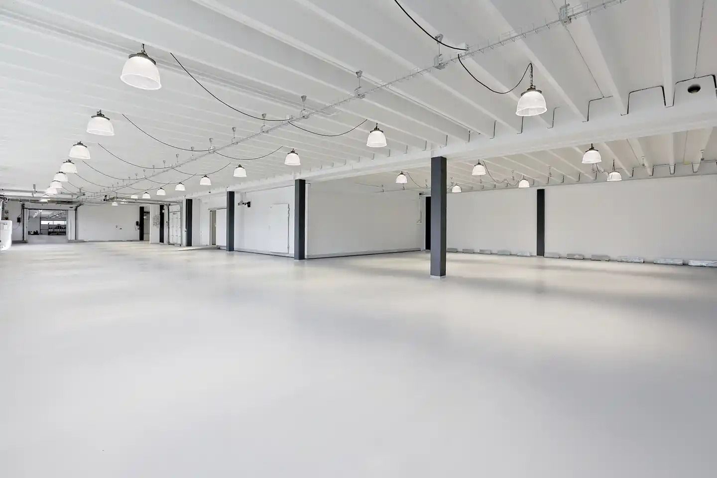 Lagerlejemål med hvide vægge, gulv og loft samt flere hængelampe. Hver anden sektion har en høj, sort søjle.