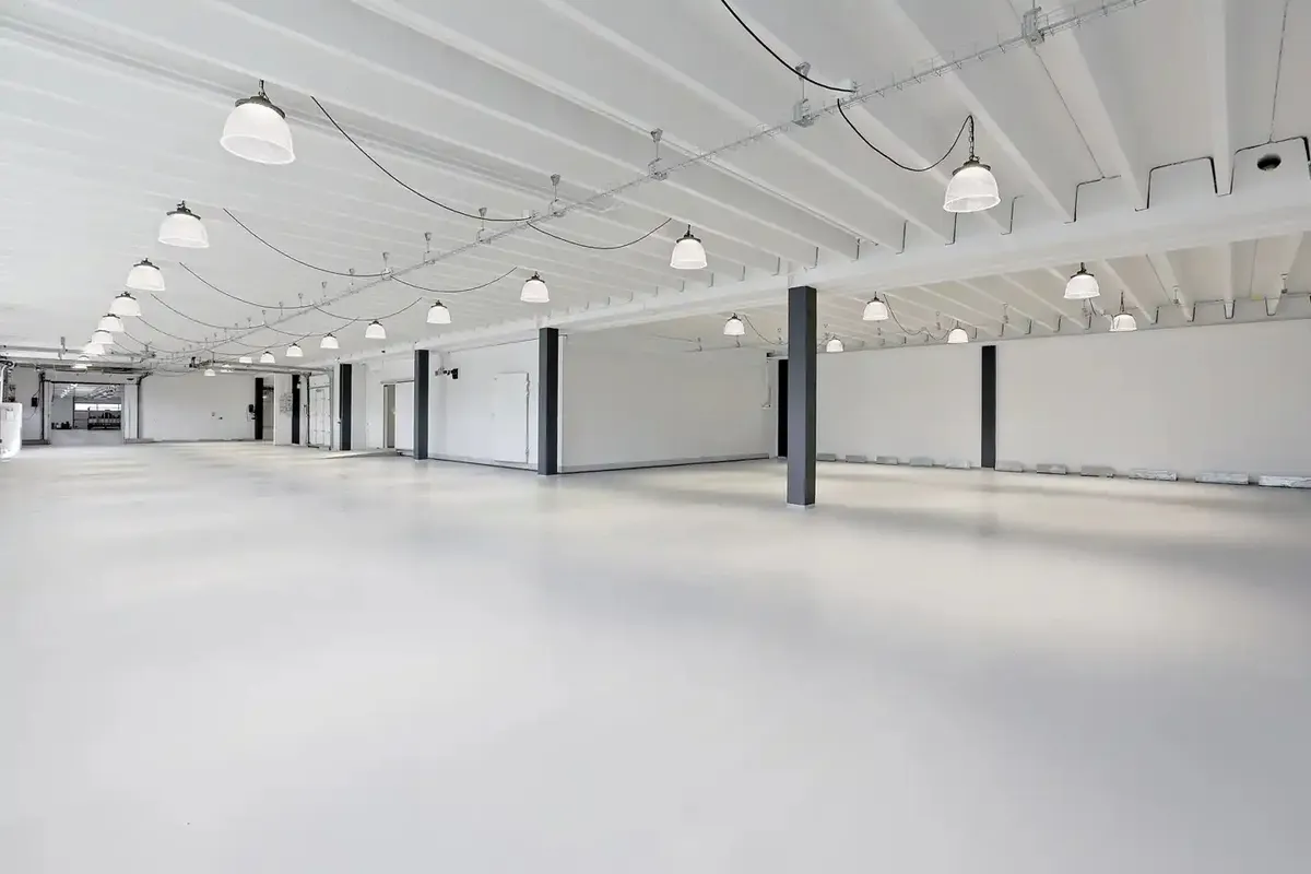 Lagerlejemål med hvide vægge, gulv og loft samt flere hængelampe. Hver anden sektion har en høj, sort søjle.