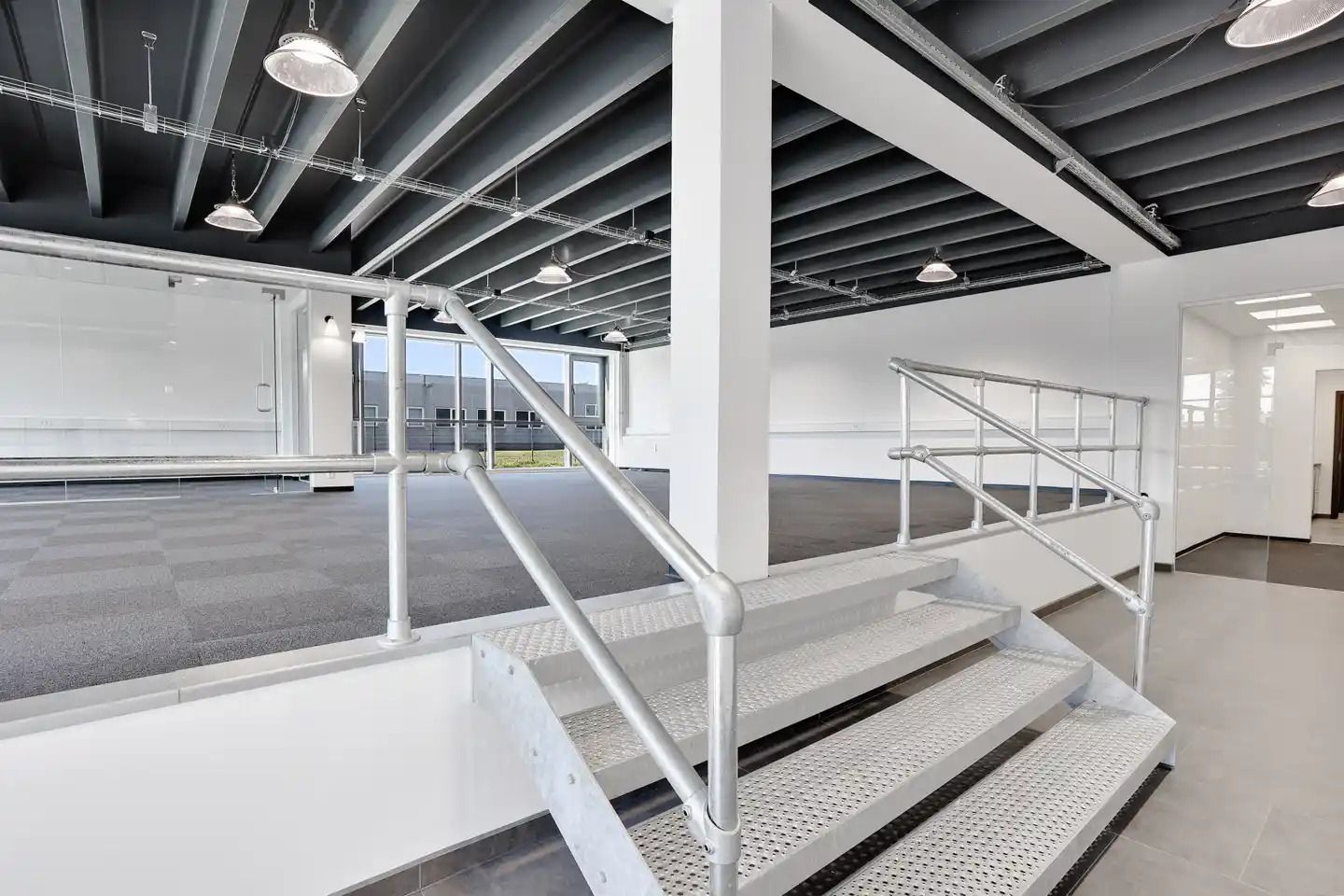 Lager med højloft, lyse buer, hvide vægge og gulv, slanke stiger og stel, metalrør og lysekroner i loftet, vinduer med glas