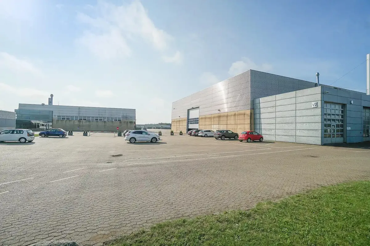 En stor industribygning med flere biler parkeret på en stor parkeringsplads med tydeligt markerede parkeringsfelter