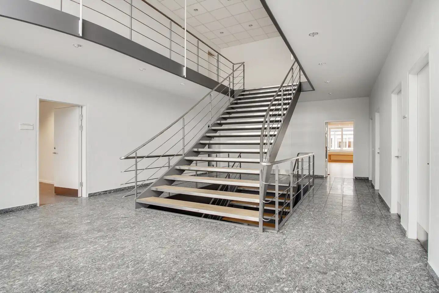 Store trapper med metalhåndtag fører op til en møbleret gang og et kontor i en ny bygning med marmorgulve