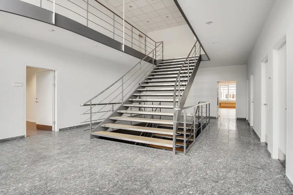 Store trapper med metalhåndtag fører op til en møbleret gang og et kontor i en ny bygning med marmorgulve
