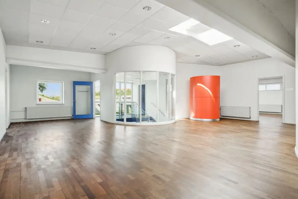 Kontorlokaler med højt til loftet og hvidt loft. Værelse med orange søjle og glasrute. Værelse med hvide vægge og blå dør.