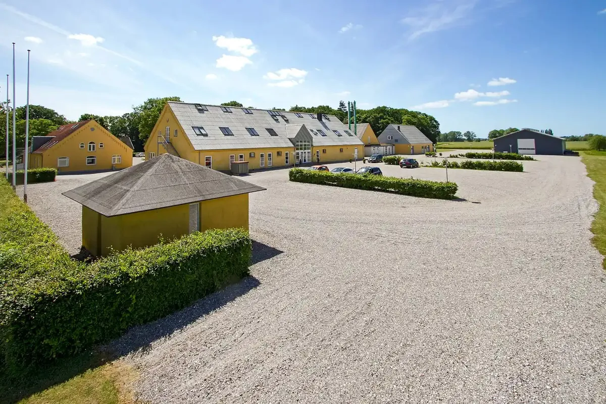 Erhvervspark med 4 bygninger med lysegul og grå farvelægning. Mange biler parkeret foran bygningerne. Et stort