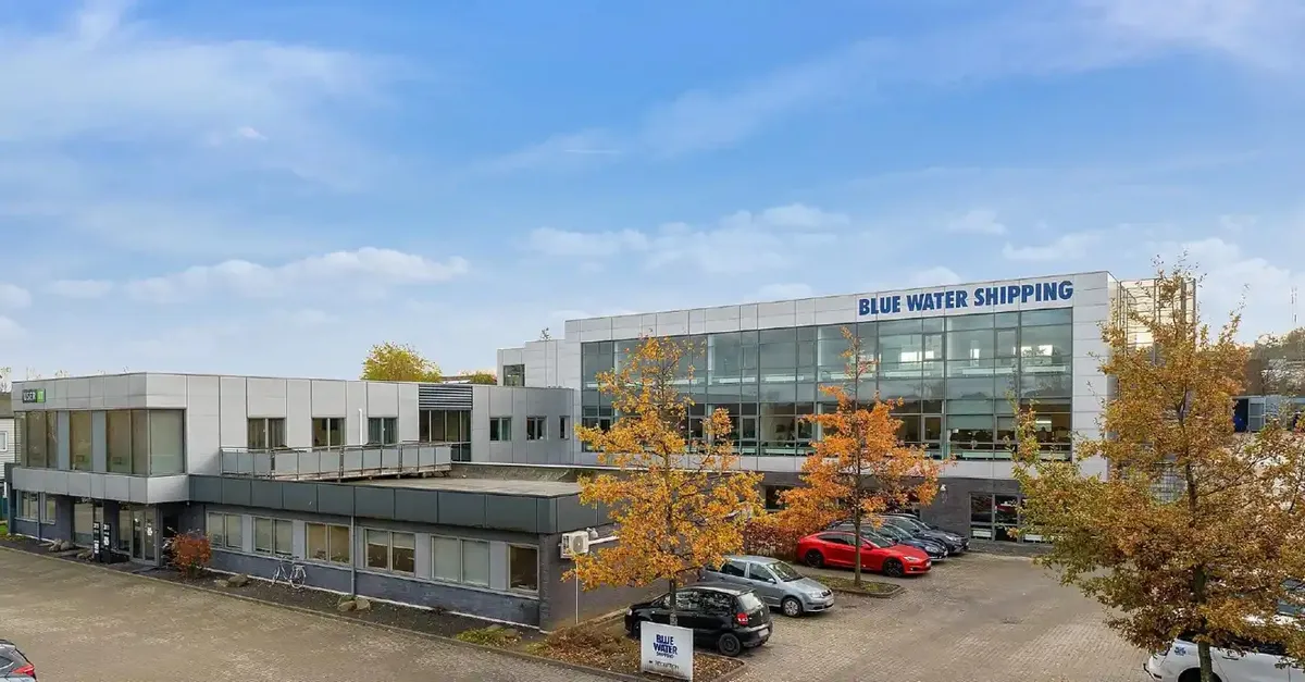 Forretningslokaler i Skejby med glasvinduer og parkerede biler, blå skilt med tekst Blue Water Shipping, træer med gule