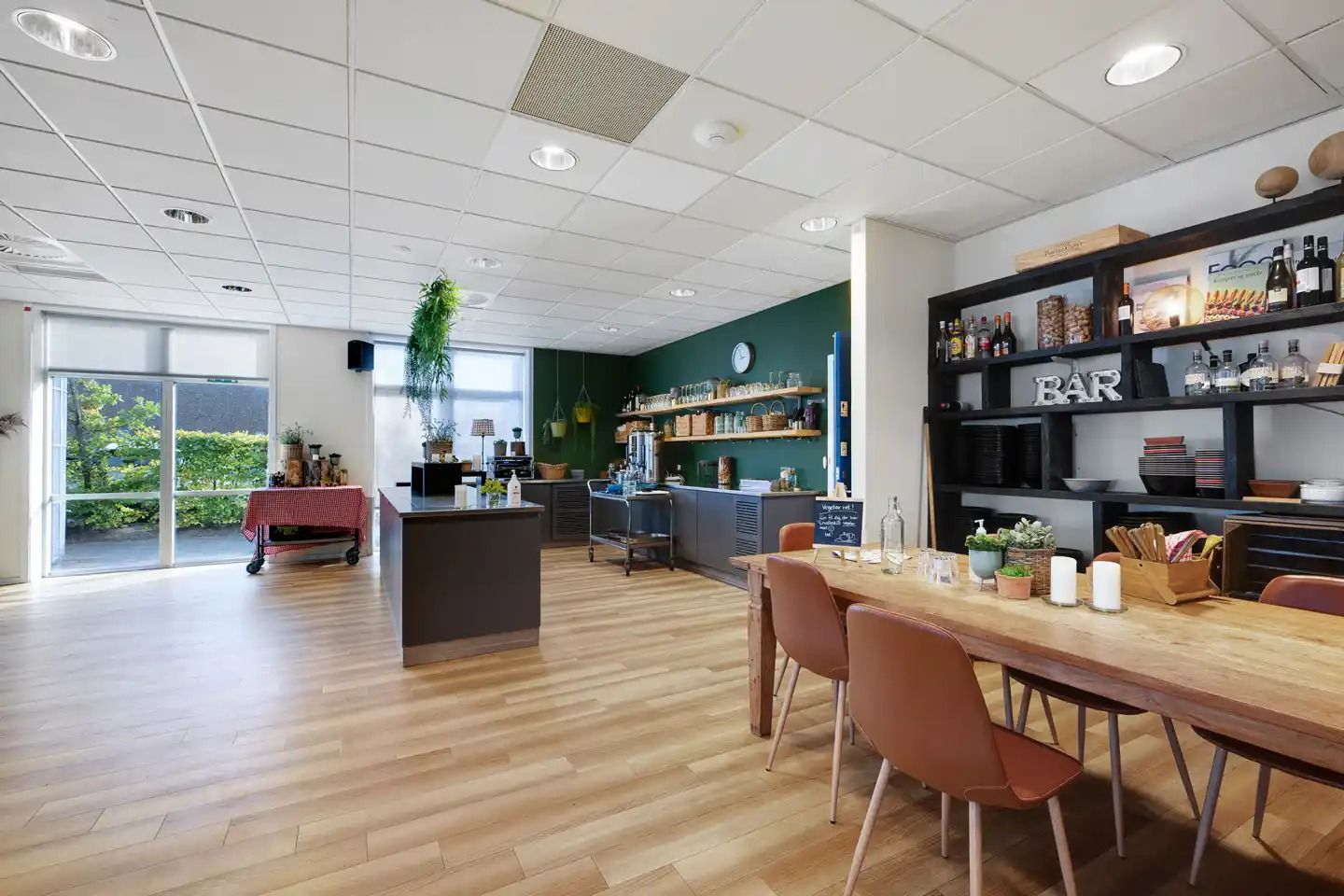 Inde i en ren og hyggelig køkkenbar med trægulv og lyse loftslampe, et bord med lysebrune stole og en væg med grøn maling og