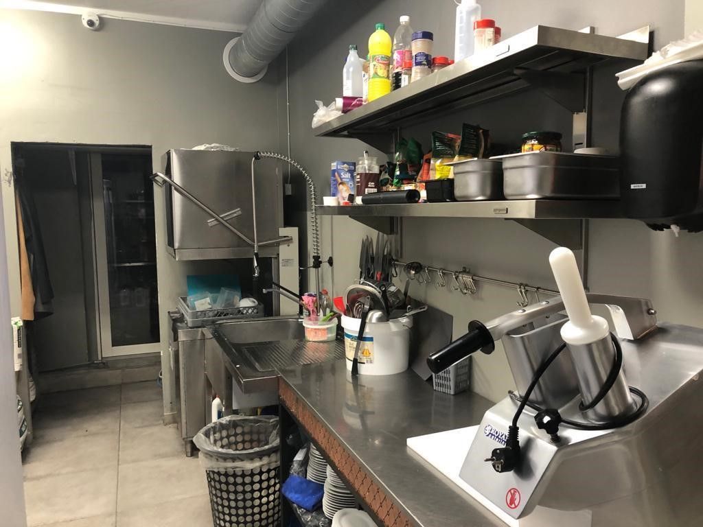 Et fuldt udstyret cateringskøkken med flere køleskabe, en vaskemaskine, et køleskab og en gryde. Der er også et servierhylde