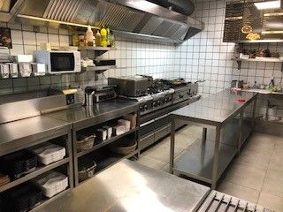 En moderne og fuldt udstyret cateringskøkken med flere apparater, et køleskab og en stor kogeplade