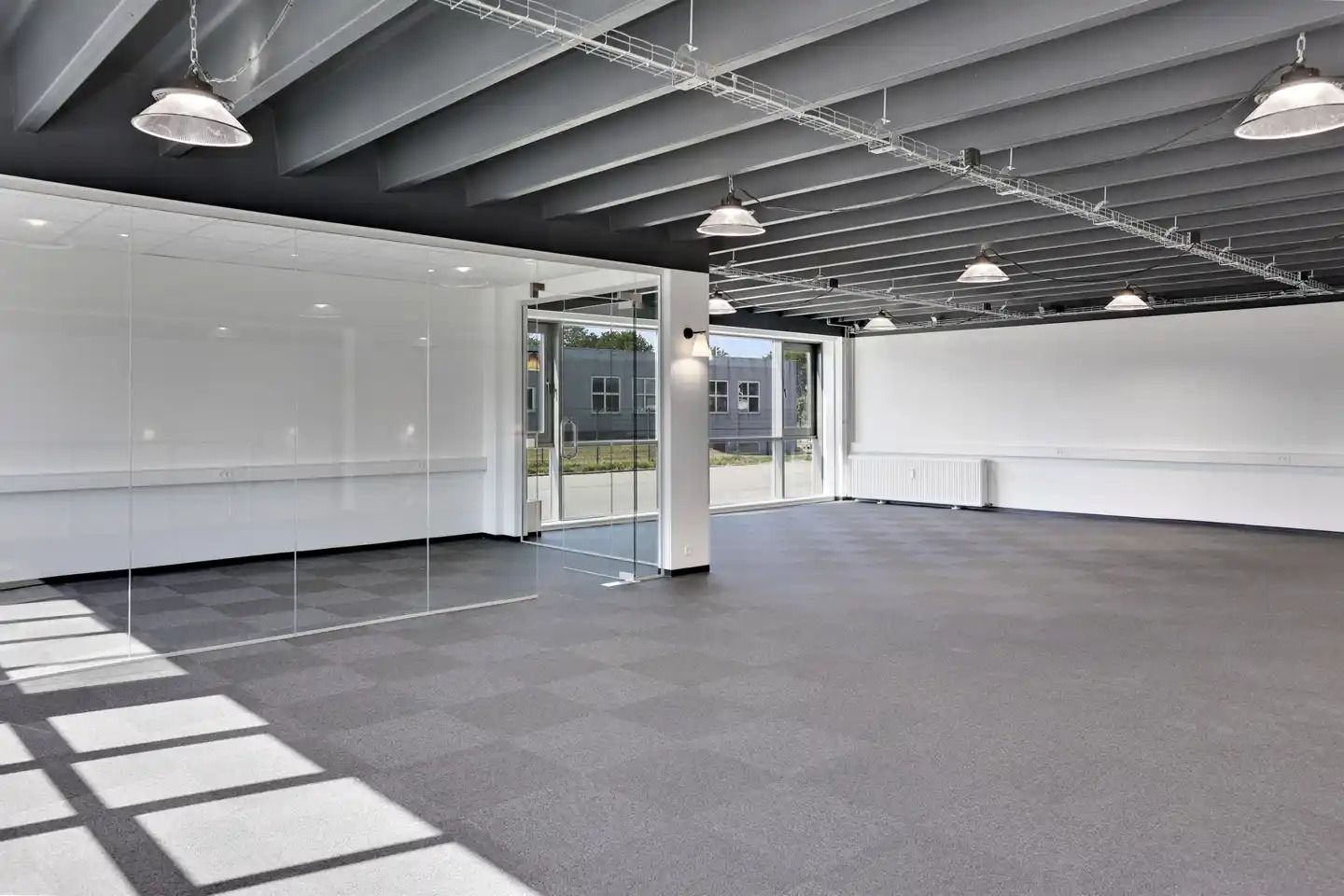 Rummelig lagerlejemål med store glasruder og højloftede rum. Moderne indretning med hvide vægge og lyse loftslampe.
