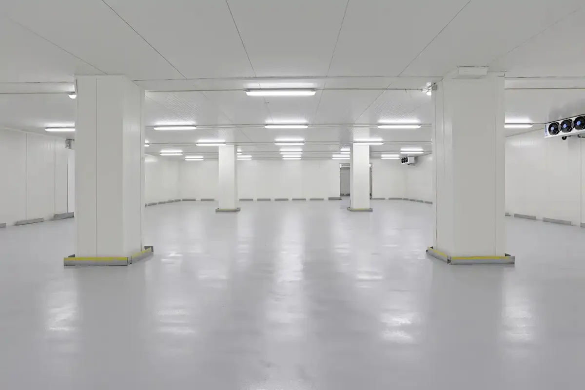 En stor og rummelig kølelagerhal med lysegul gulvbelægning og flere store hvide søjler fordelt rundt i rummet