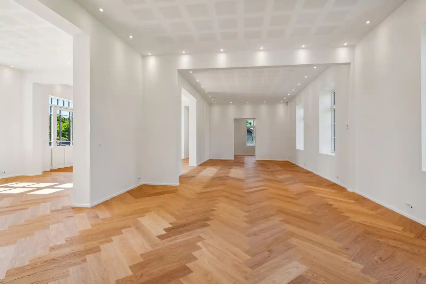 En stor og lyse kontorhjørne med hvide vægge og trægulv, samt hvide loftsbelægninger med indbygget belysning og åbne vinduer