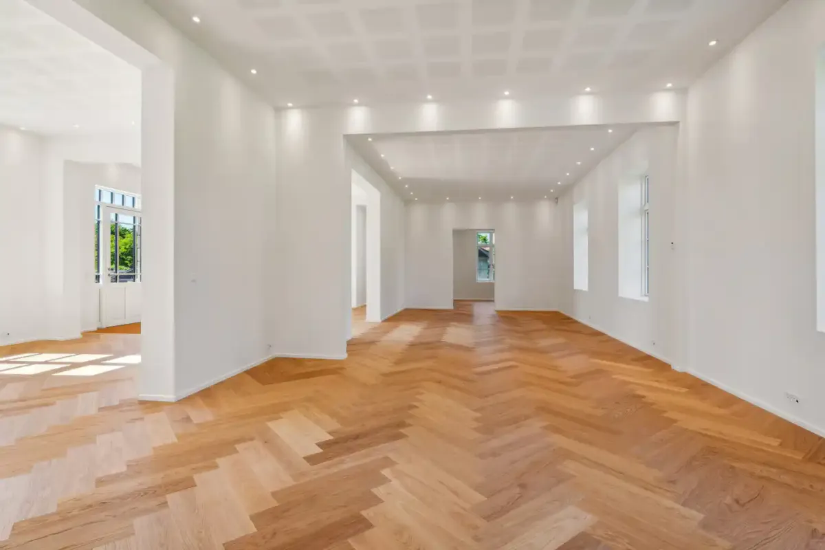 En stor og lyse kontorhjørne med hvide vægge og trægulv, samt hvide loftsbelægninger med indbygget belysning og åbne vinduer