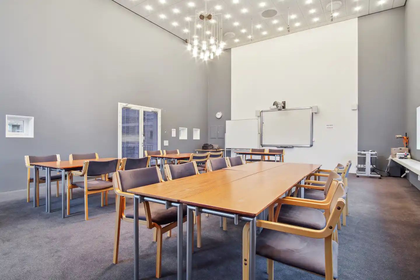 En stor konferencesal med borde og stole, der er ordnet rundt om en stor hvidt kridttavle og et gulvmonteret ure
