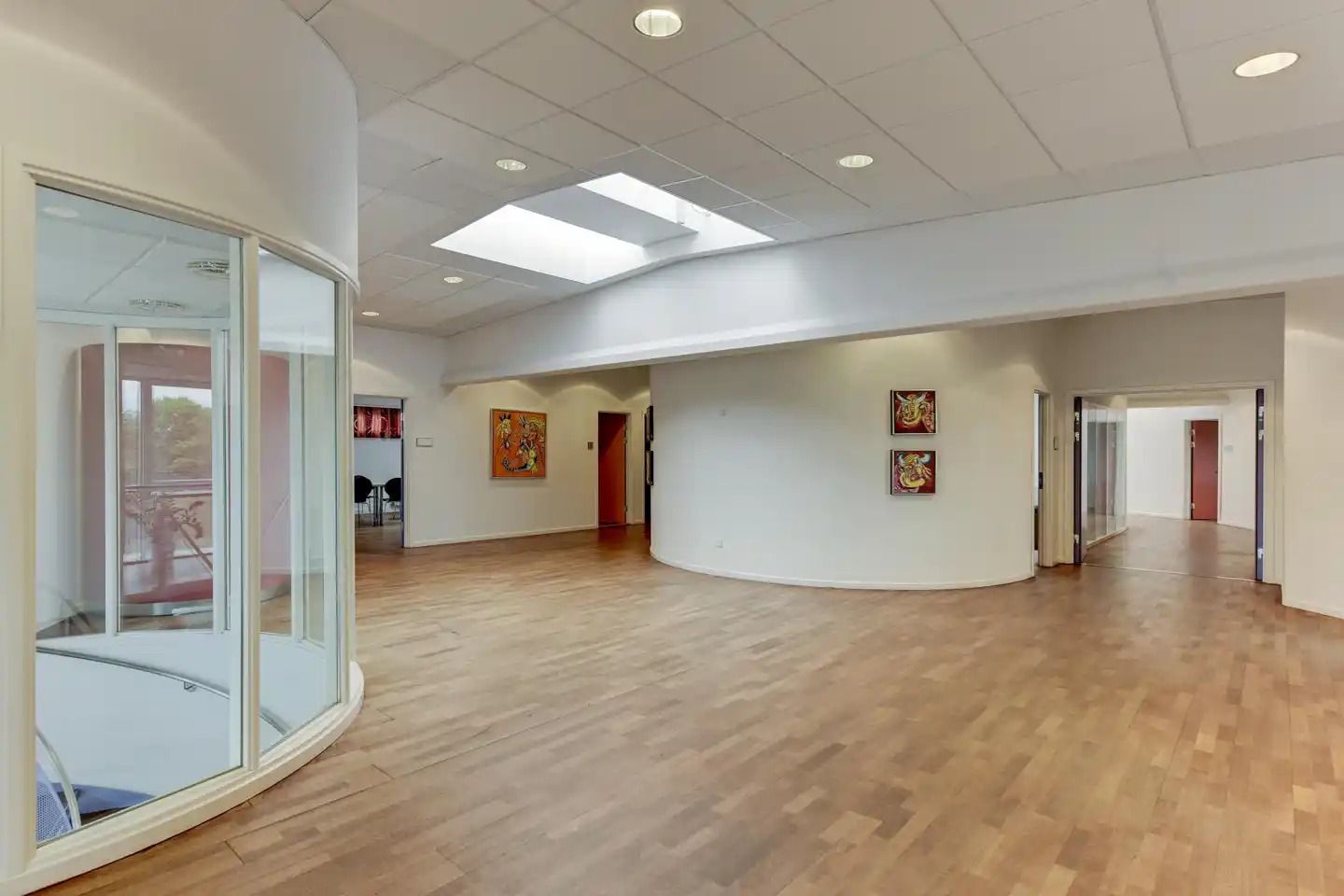 En stor, lys og moderne kontorhal med lyse lofter, store vinduer og flotte trægulve. To malerier er hængt op på væggen og