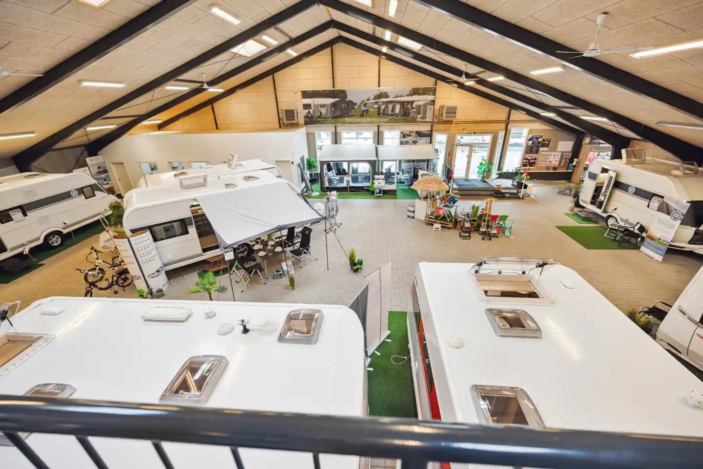 Store hvide trailere med røde og hvide skilte er udstillet på et lager med loftsventilatorer og gulvbelægning.