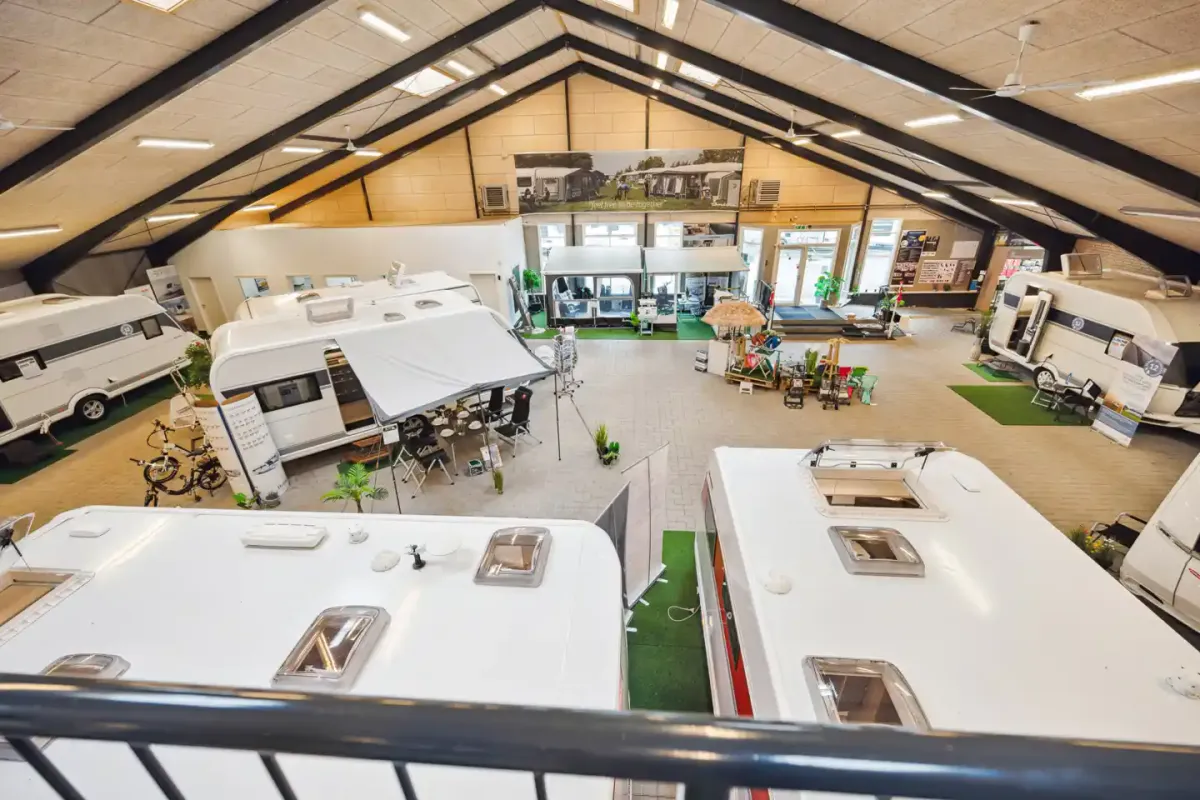 Store hvide trailere med røde og hvide skilte er udstillet på et lager med loftsventilatorer og gulvbelægning.