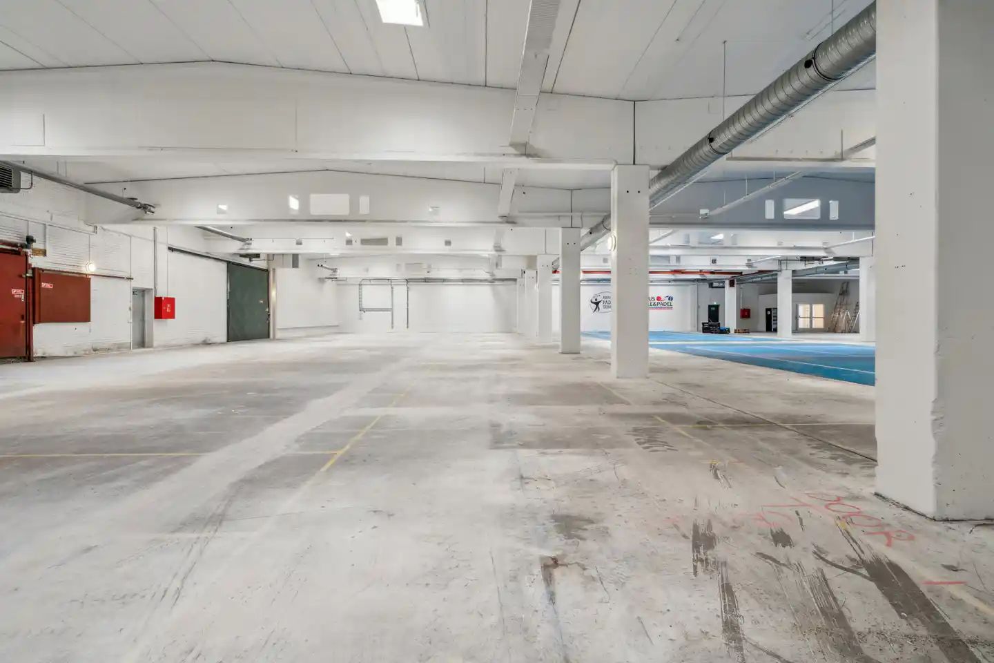 Lager med en stor åben rum, gulv, hvide vægge og store støtter, der går fra gulv til loft samt røg og skrift på gulvet