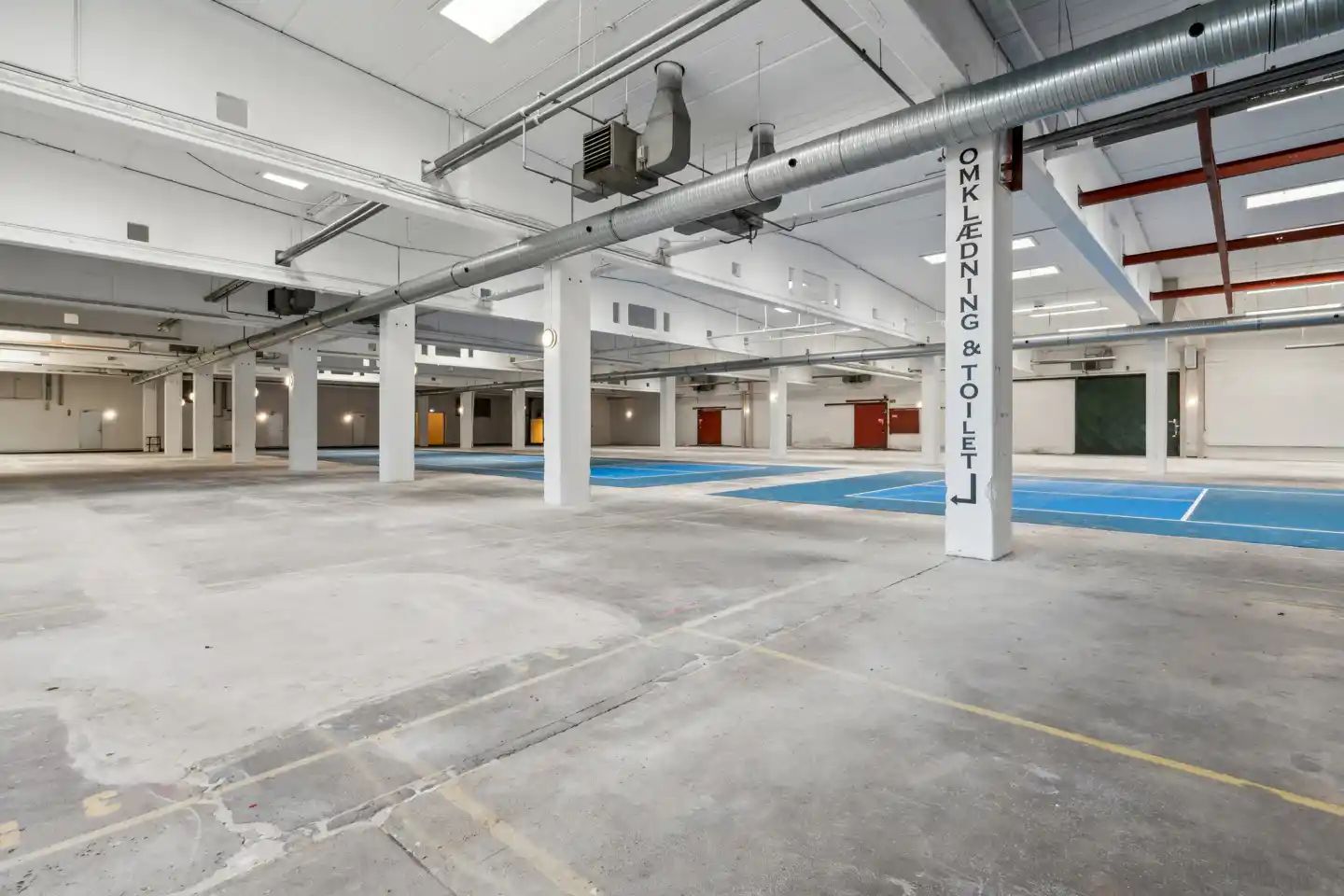 Lager med højt til loftet, flere lagerrum, toilet og omklædningsrum, lysegul og blå gulvbelægning og hvidt loft.