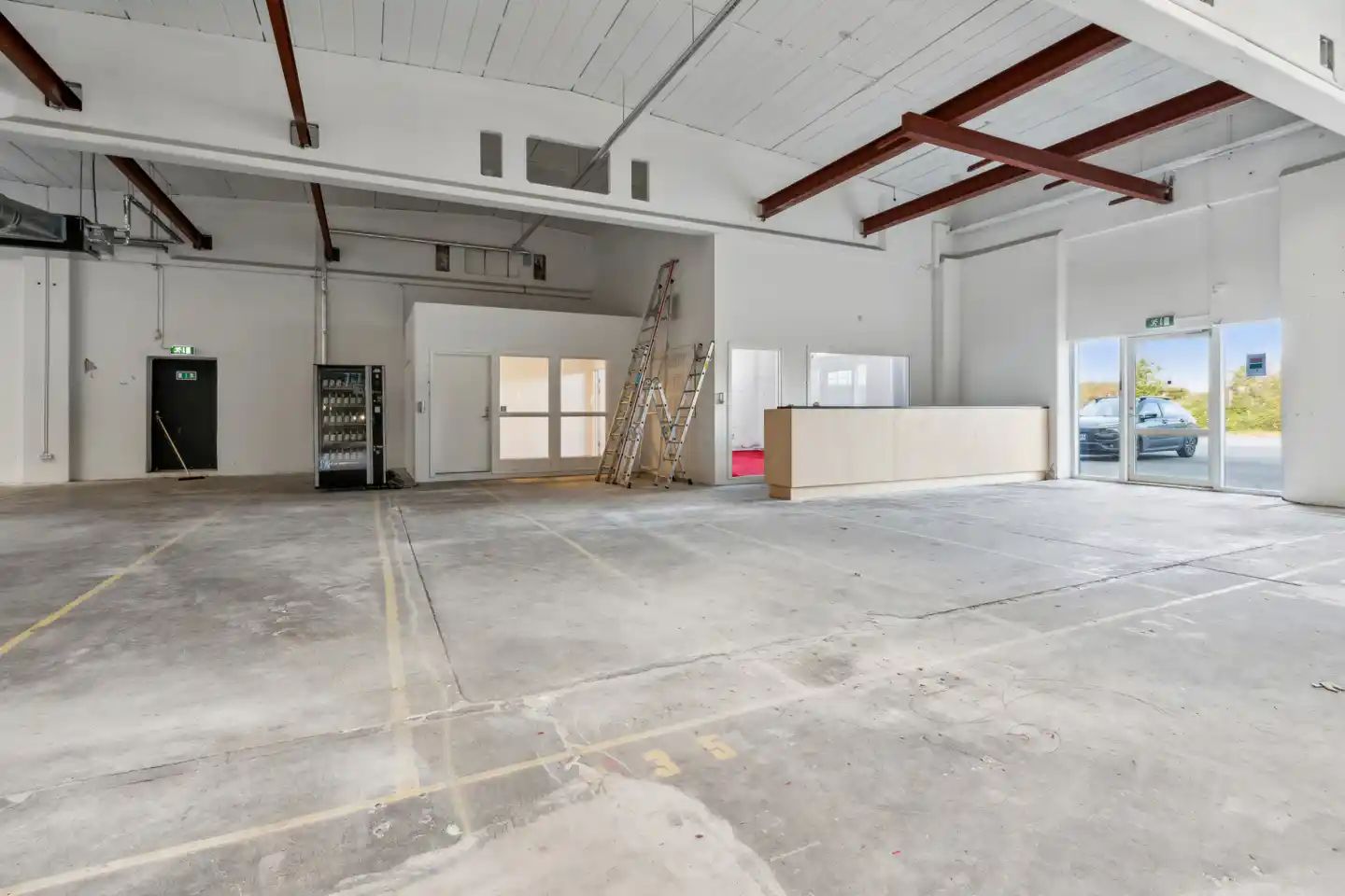 Lagerlokaler med en stor åbning til indkørsel og to vinduer samt stige og en søjle til højre samt en indre dør til venstre