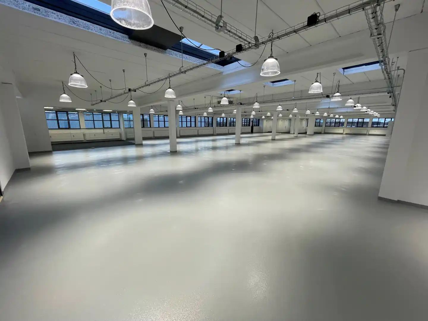 Et rum med hvide vægge og lofter, store vinduer, hængende lysekroner, og en stor åben gulvplads.