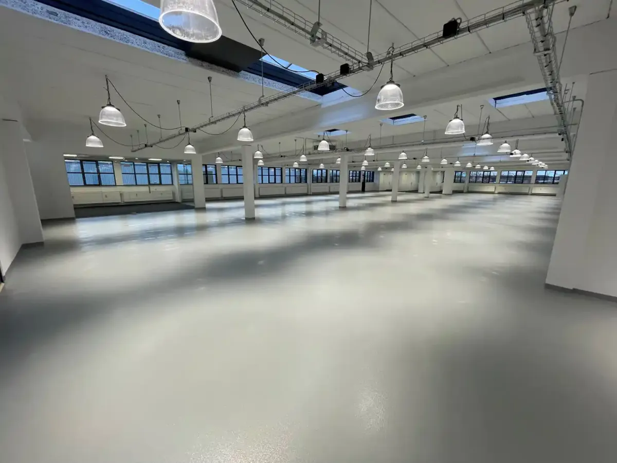 Et rum med hvide vægge og lofter, store vinduer, hængende lysekroner, og en stor åben gulvplads.