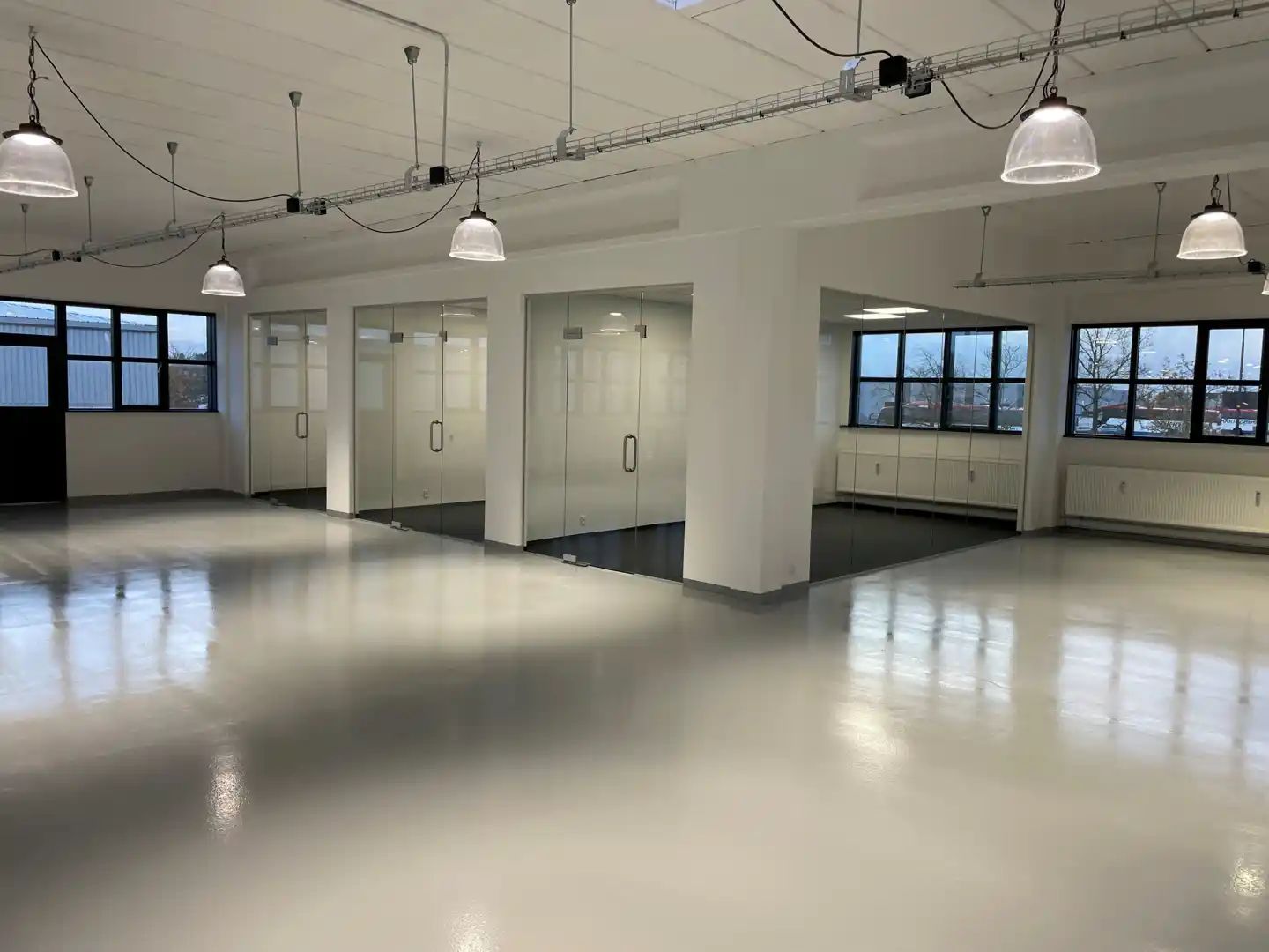 Moderne og rummelig kontor med store vinduer, glasdøre, hvide vægge, lyse gulve og hængende lamper