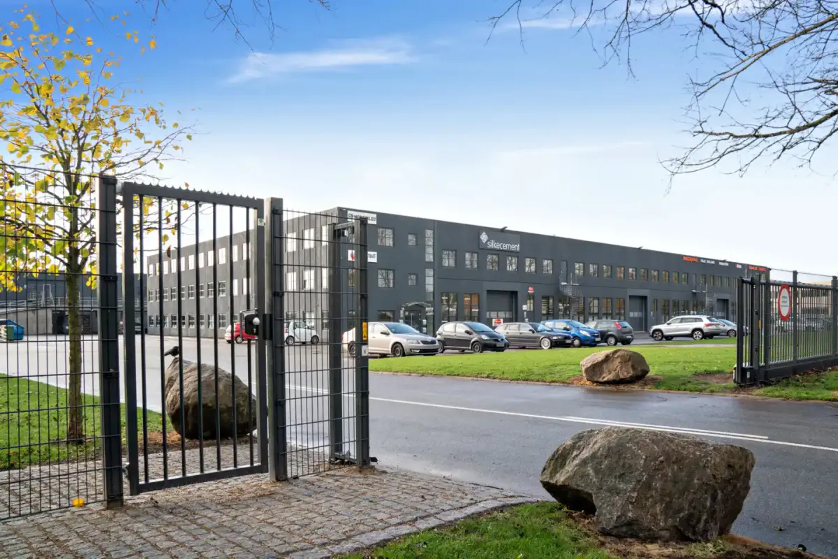 Et moderne kontorbyggeri med mange vinduer og et indre parkeringsområde med biler parkeret på en asfaltvej