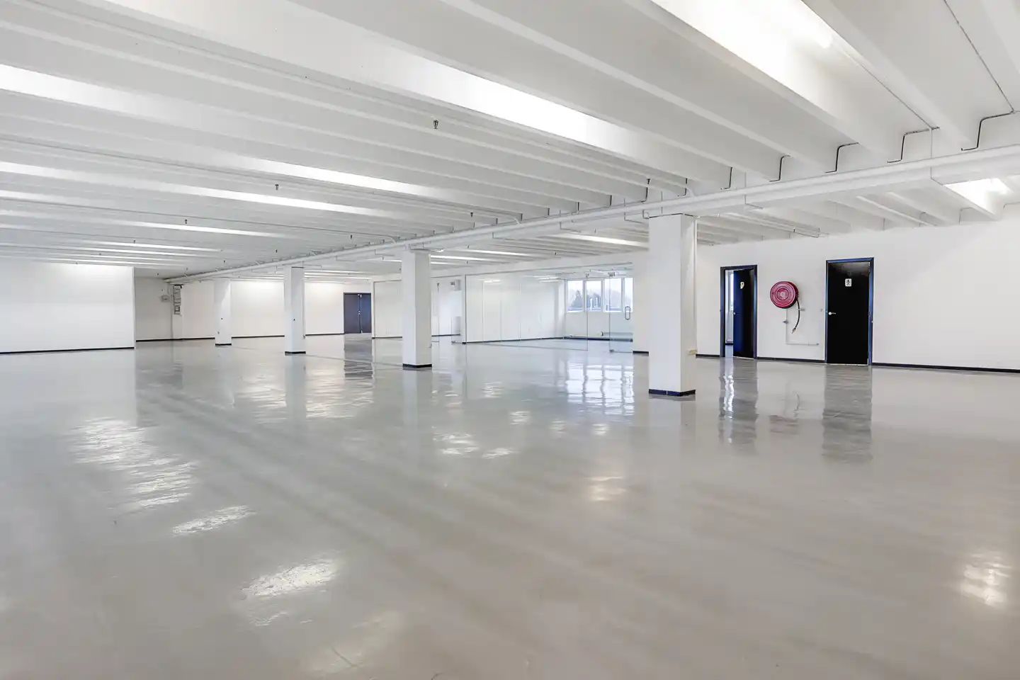 En stor hall med hvide vægge og lofter, lyse gulv og tæt tæt afstand mellem søjler og døre