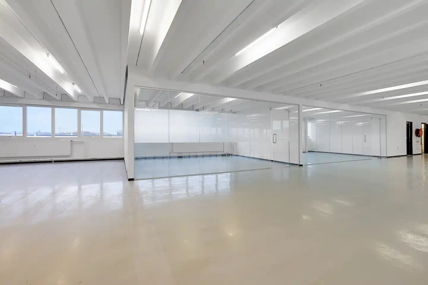 Et stort kontorlokal med hvide vægge, højt til loftet og glasvægge og døre