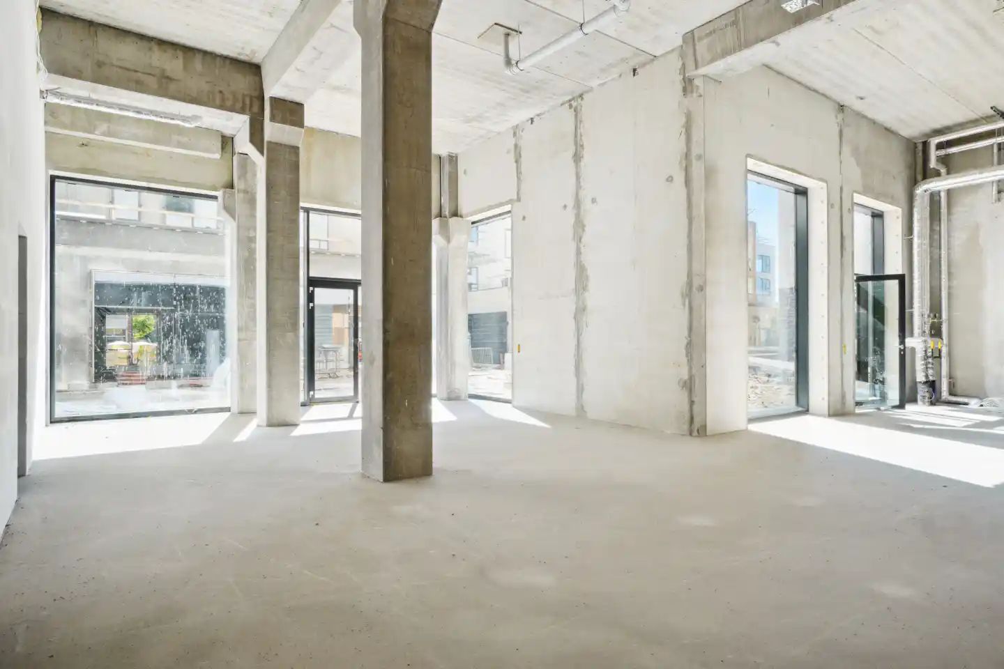 En stor, tom og hvid malet lokale med højt til loftet, store vinduer og to stærke søjler i midten